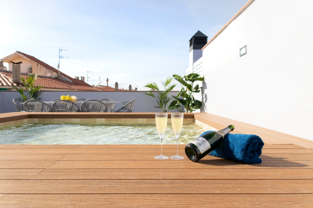 Bottle of champagne and a towel on the wooden decking surrounding the jacuzzi pool at Calafell Home Apartments.