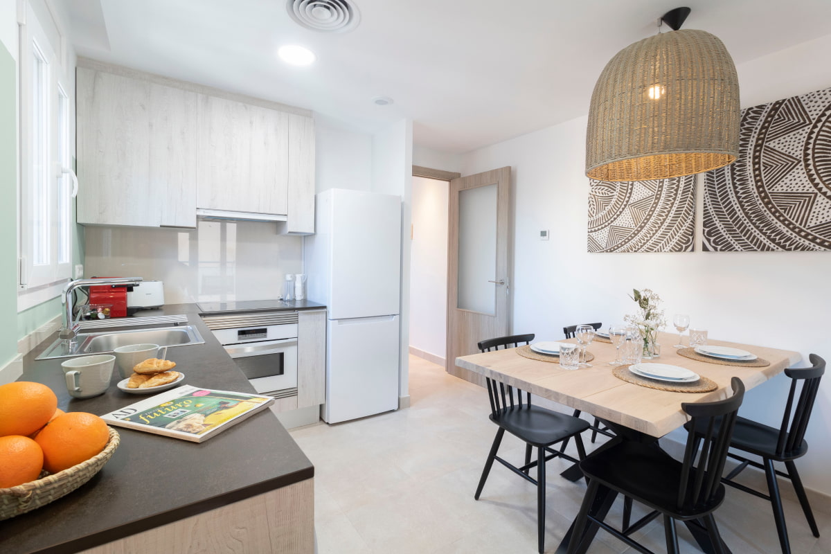 Kitchen in one of the apartments at Calafell Home Apartments, featuring a fridge, oven, and wicker lamp.