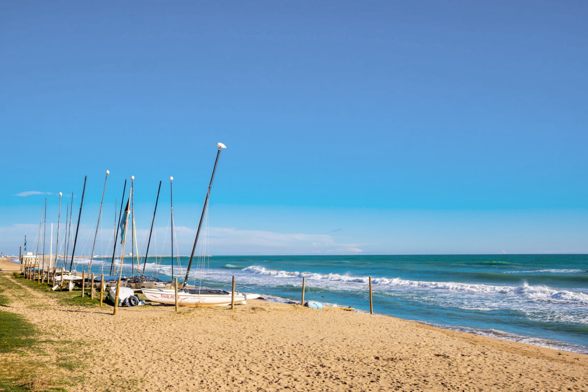 Sandy beach with several anchored boats under a clear and calm sky, perfect for a day of relaxation.