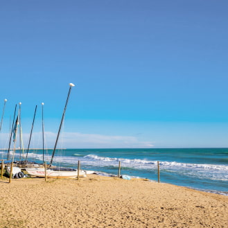 Sandy beach with several anchored boats under a clear and calm sky, perfect for a day of relaxation.