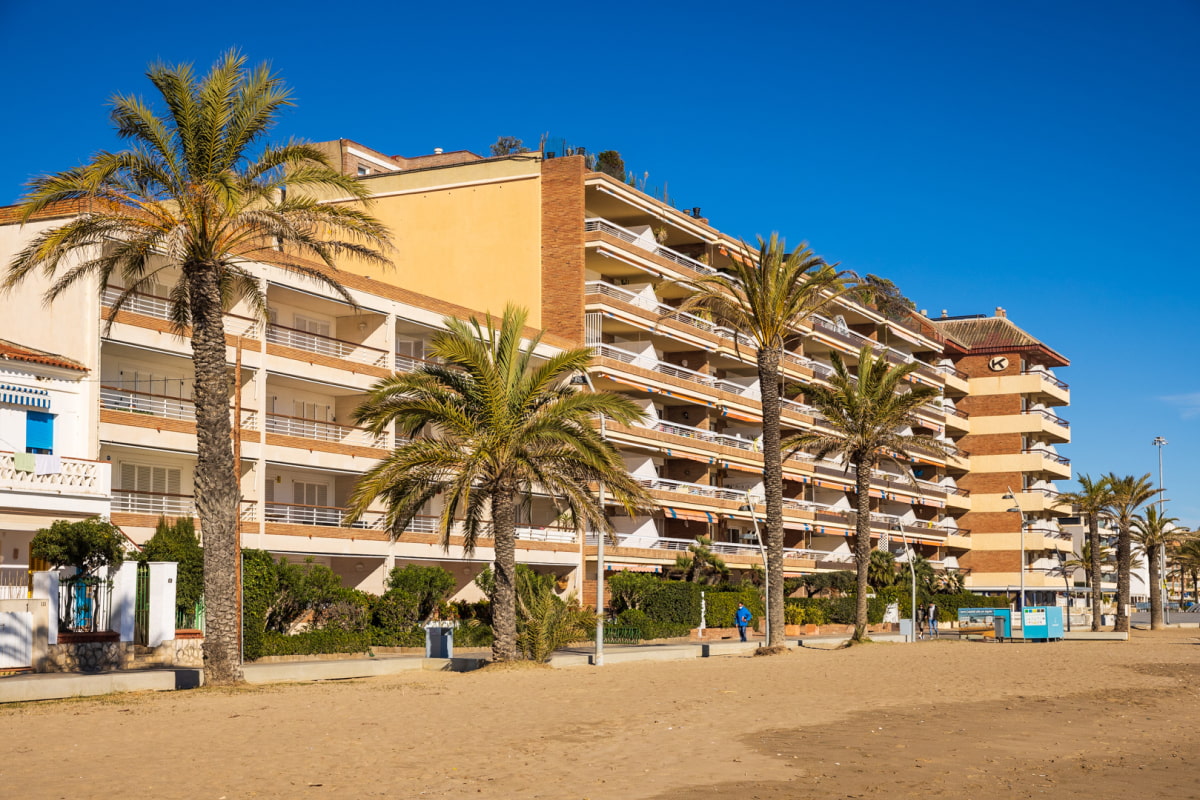 Promenade along Calafell Beach, flanked by buildings and palm trees.