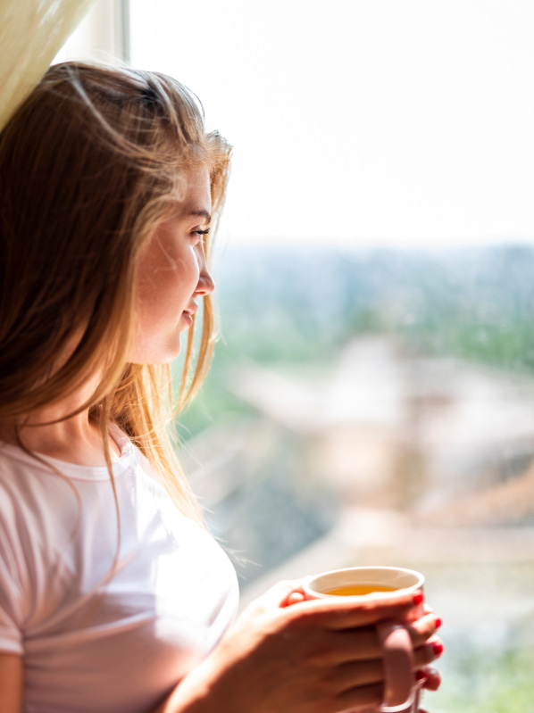 Persona asomándose a una venta con un té caliente en la mano